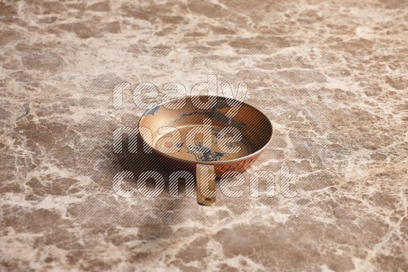 A small copper pan on beige marble background