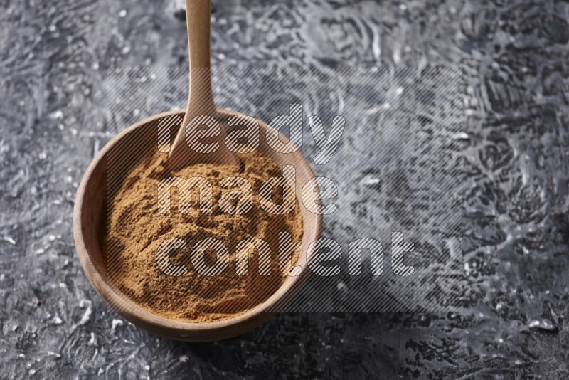 Wooden bowl full of cinnamon powder with a wooden spoon on a textured black background in different angles