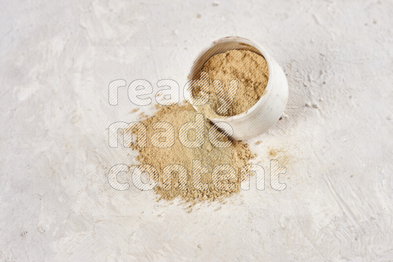 A beige pottery bowl full of ground ginger powder with fallen powder from it on white background