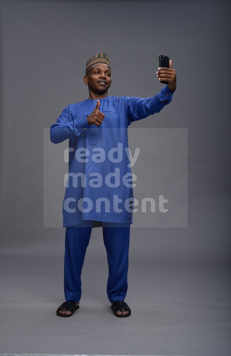 Man wearing Nigerian outfit standing taking selfie on gray background
