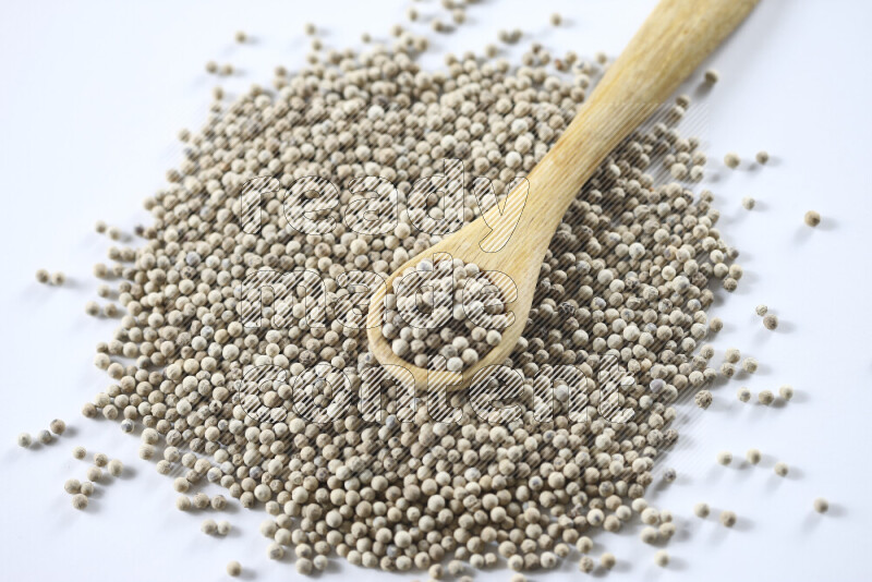 حبوب الفلفل الأبيض مع ملعقة خشبية علي خلفية بيضاء