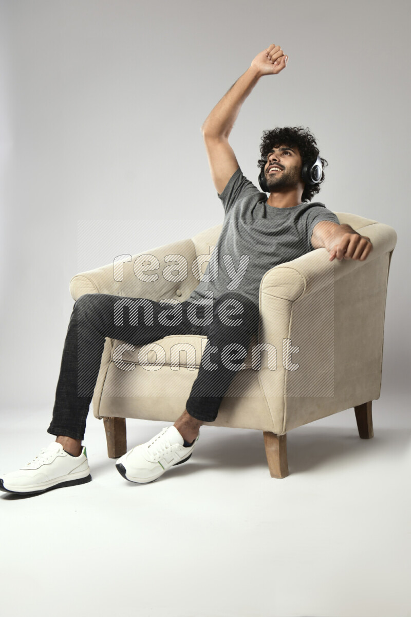 A man wearing casual sitting on a chair putting on headphones on white background