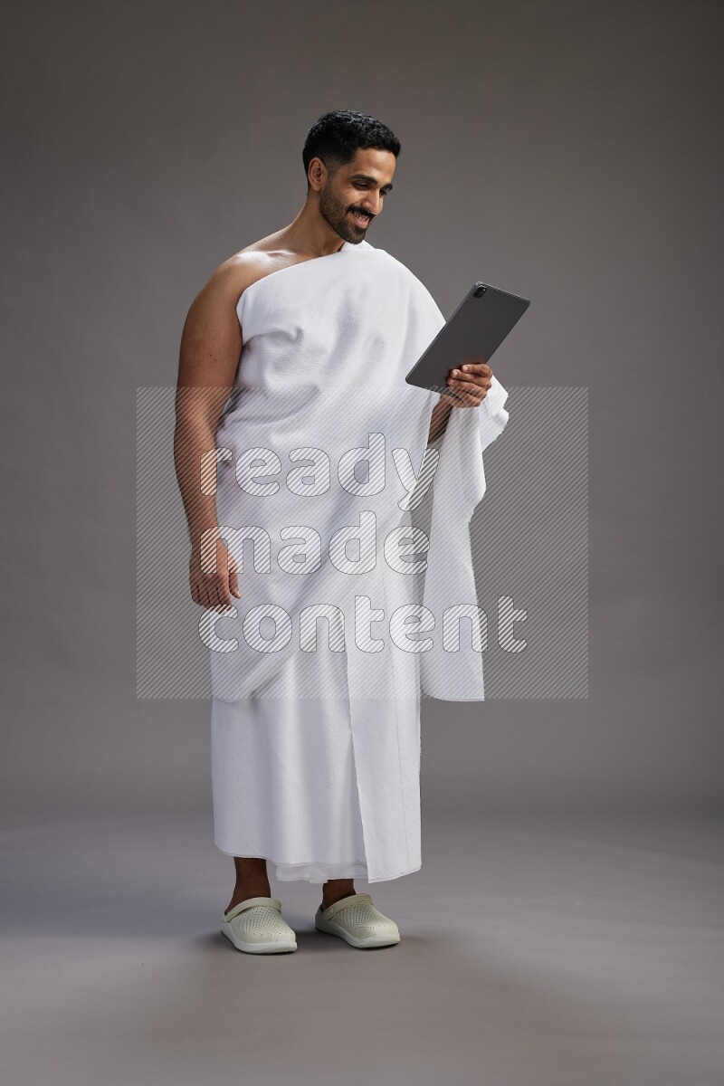 A man wearing Ehram and holding a tablet on gray background
