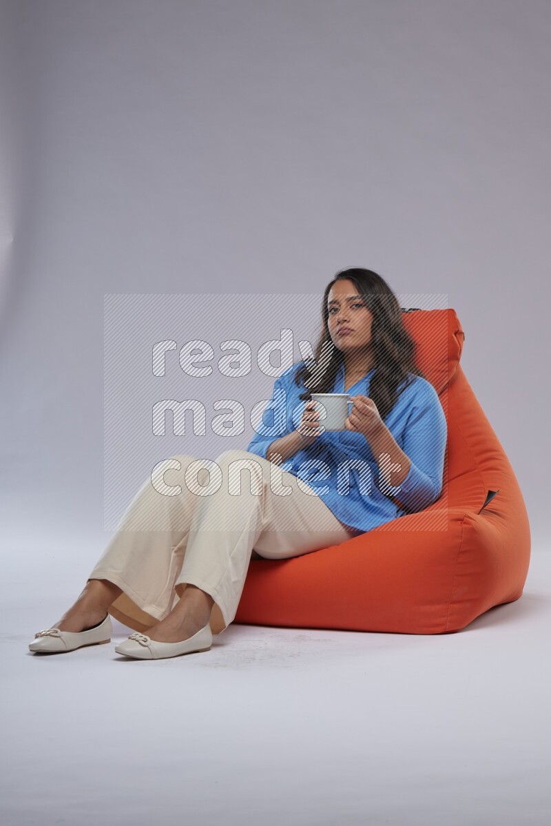 A woman sitting on an orange beanbag and drinking coffee