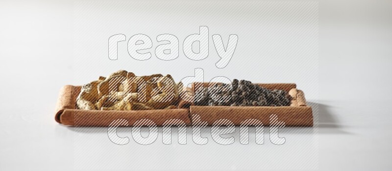 مربعان من أعواد القرفة ممتلئان بحبوب الفلفل الأسود وأصابع الكركم علي خلفية بيضاء