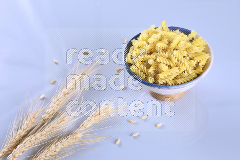 Raw pasta with wheat stalks on light blue background