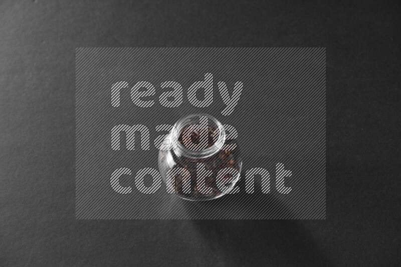 A glass spice jar full of cloves on black flooring
