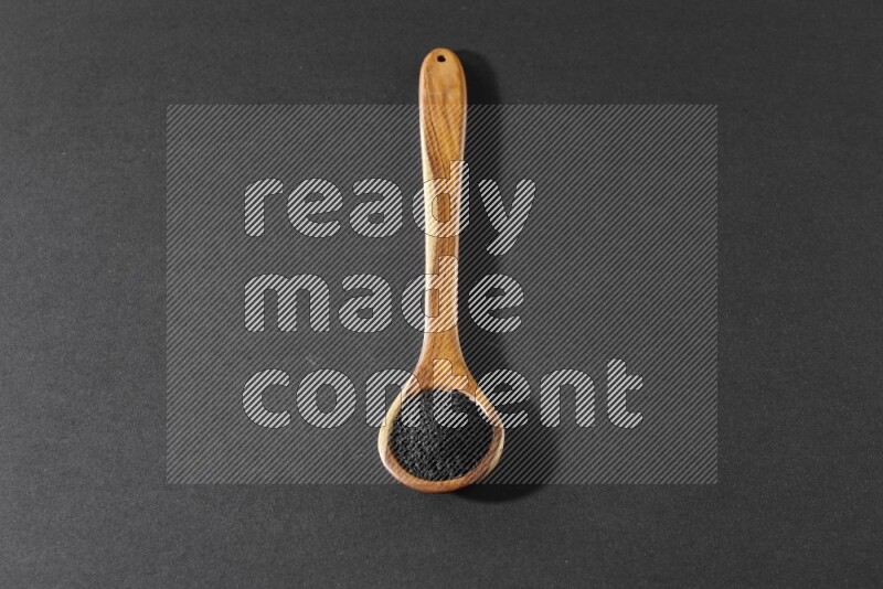 A wooden ladle full of black seeds on a black flooring