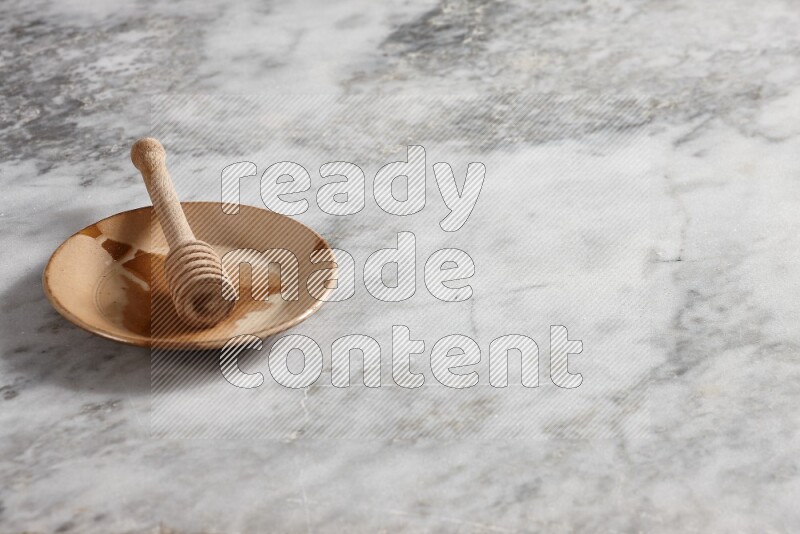Multicolored pottery plate with wooden honey dipper in it on grey marble background