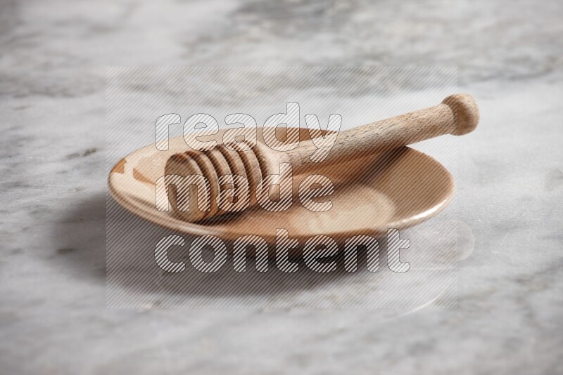 Multicolored pottery plate with wooden honey dipper in it on grey marble background