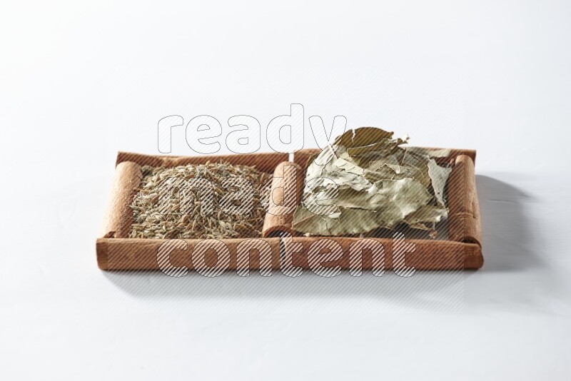 مربعان من أعواد القرفة ممتلئان بأوراق الغار والكمون علي خلفية بيضاء