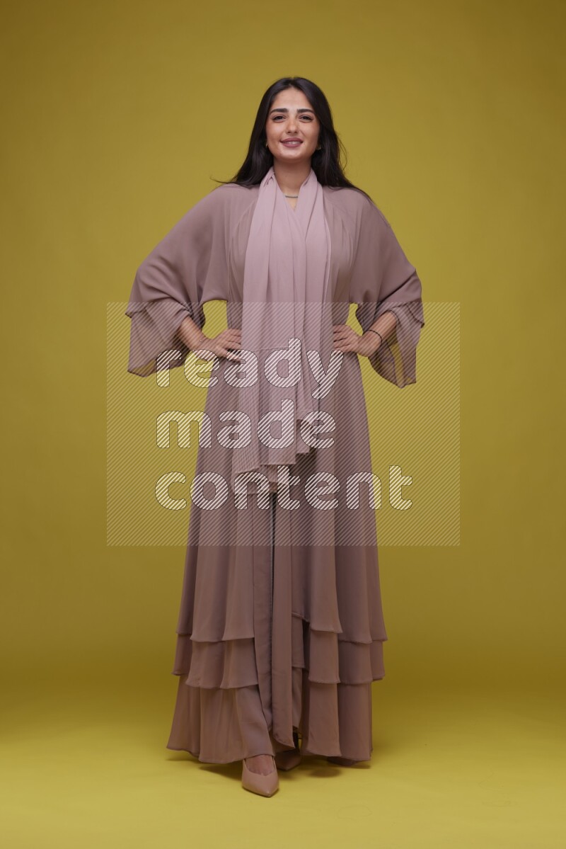 A woman Posing on a Yellow Background wearing Brown Abaya