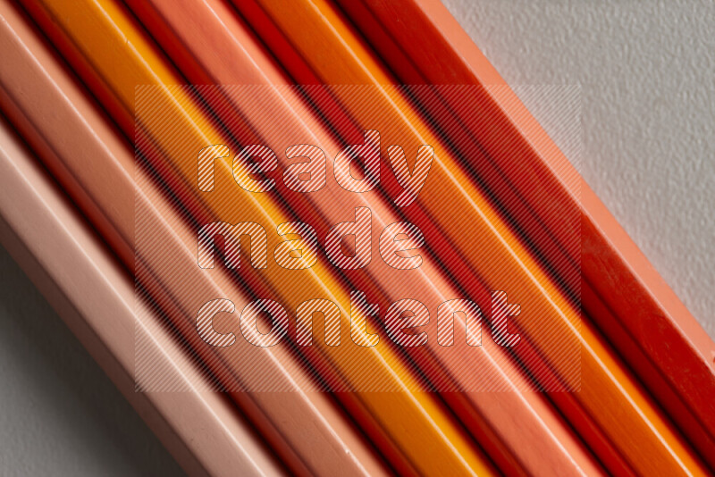 A collection of colored pencils arranged showcasing a gradient of orange hues on grey background