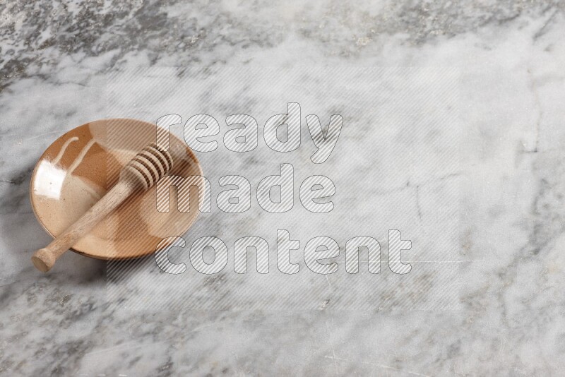 Multicolored pottery plate with wooden honey dipper in it on grey marble background