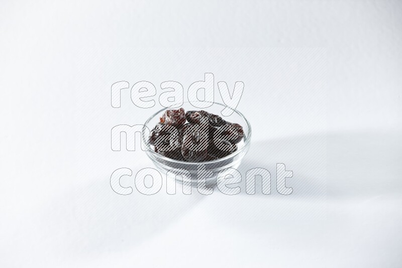 A glass bowl full of dried plums on a white background in different angles