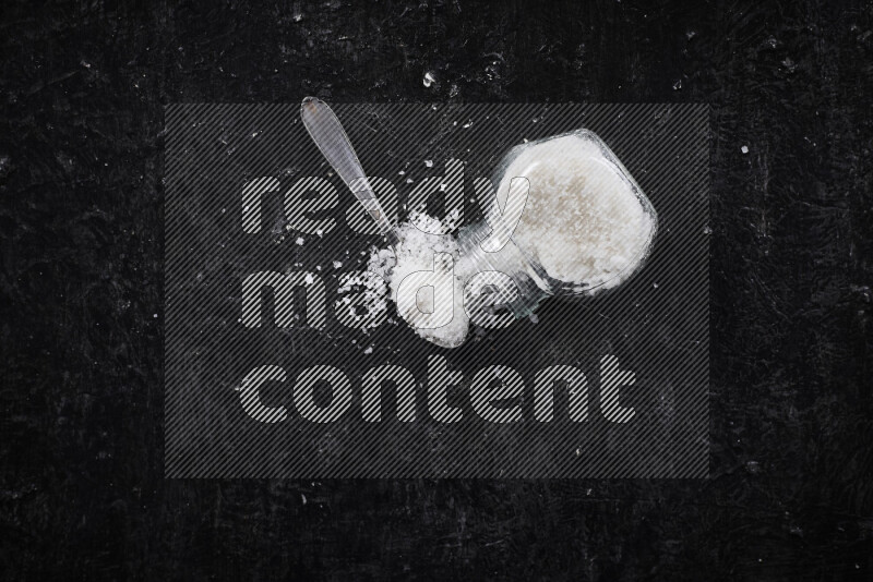 A glass jar full of coarse sea salt crystals on black background