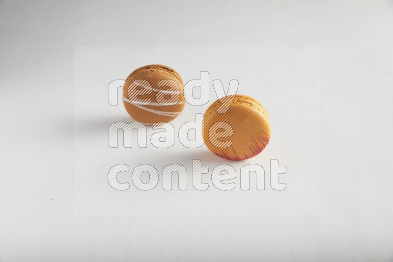 45º Shot of of two assorted Brown Irish Cream, and Orange Exotic macarons on white background
