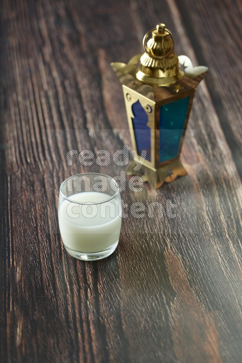 A golden lantern with different drinks, dates, nuts, prayer beads and quran on brown wooden background