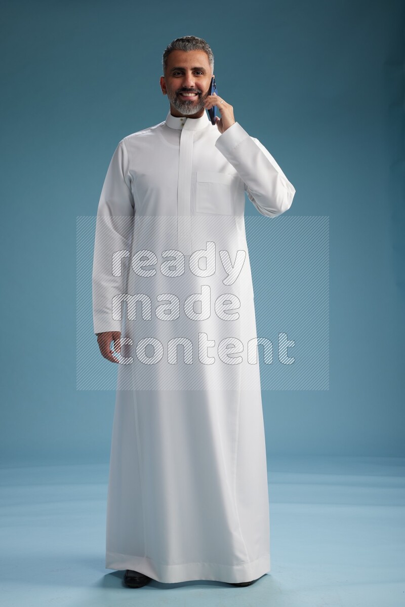 Saudi man wearing thob talking on the phone on blue background