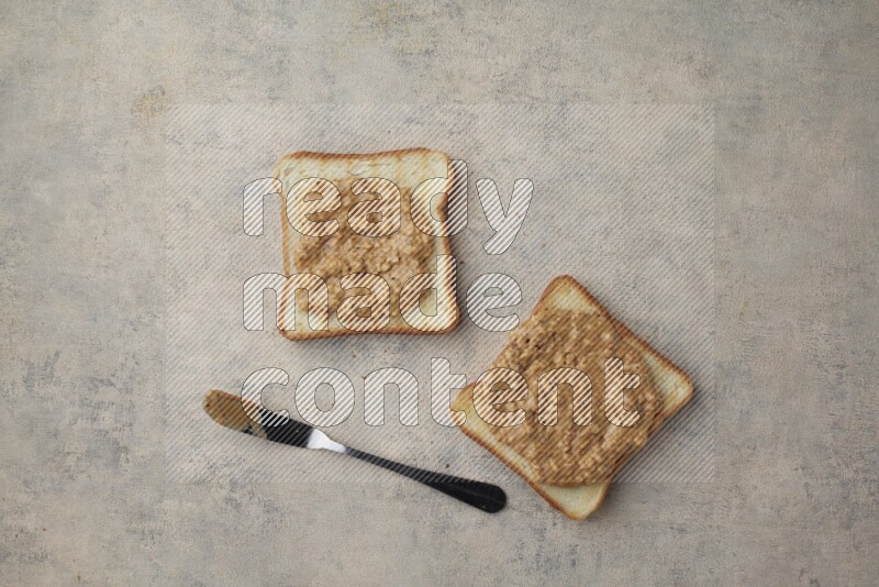 Crunchy  peanut butter on a toasted white toast slices with a spreading knife on a light blue textured background