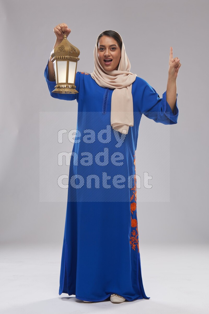 A Saudi woman standing wearing Jalabeya holding a lantern