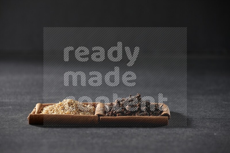 مربعان من أعواد القرفة ممتلئان ببذور السمسم والقرنفل علي خلفية سوداء