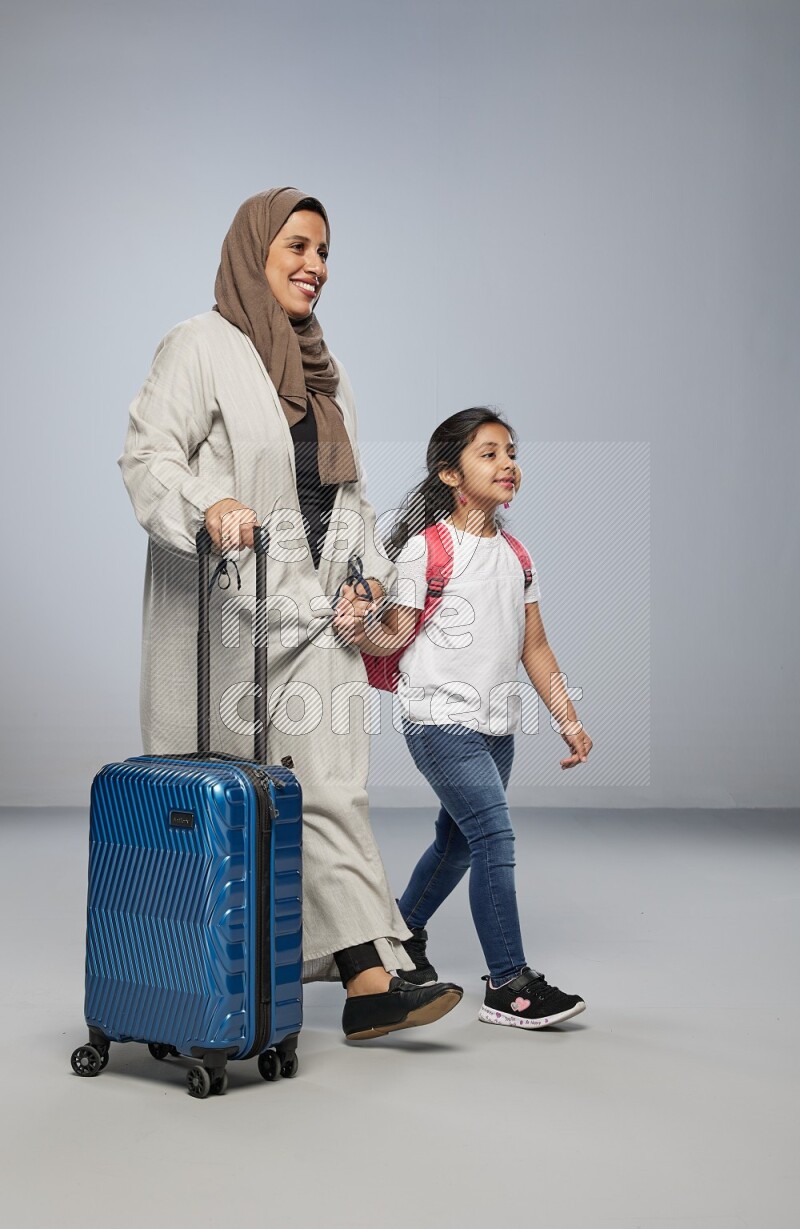 Mom and daughter standing pulling a carry-on bag on gray background
