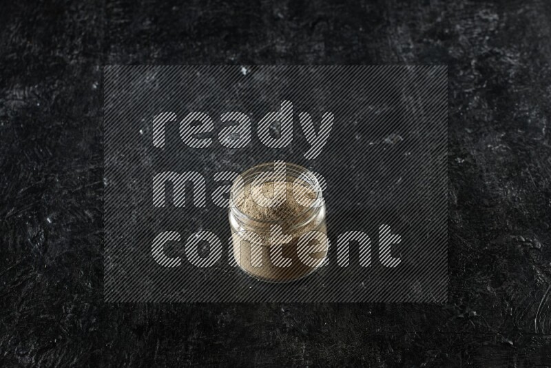 وعاء زجاجي ممتلئ ببودرة الهيل على خلفية سوداء