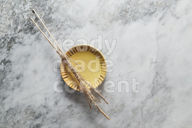 Wheat stalks on multicolored pottery plate on grey marble background
