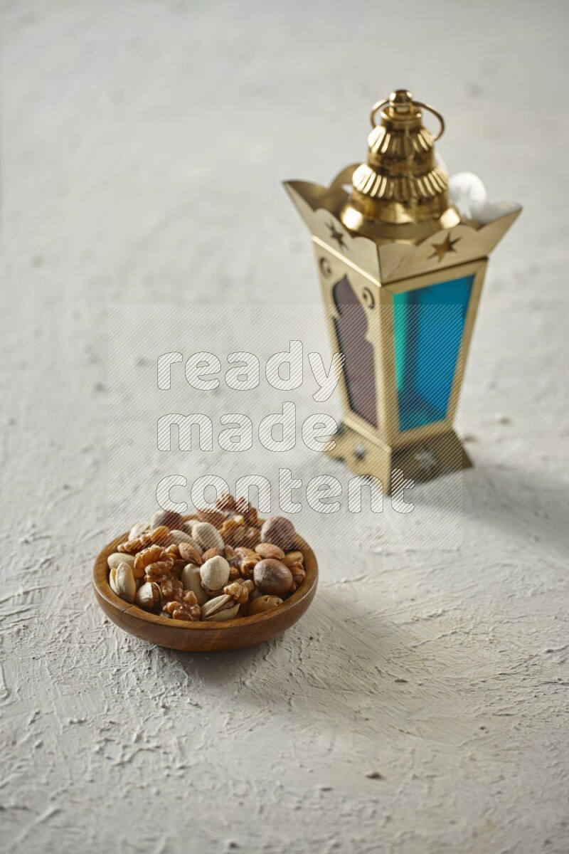 A golden lantern with different drinks, dates, nuts, prayer beads and quran on textured white background