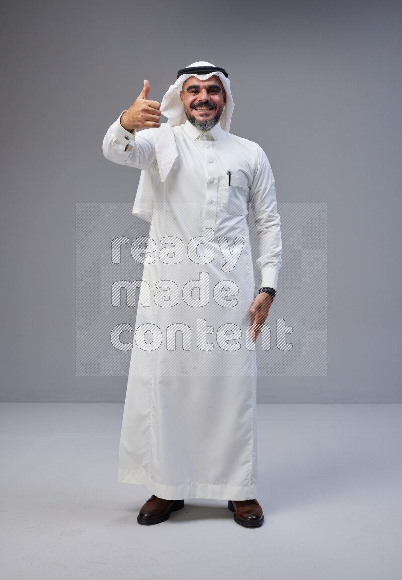 Saudi man Wearing Thob and white Shomag standing interacting with the camera on Gray background