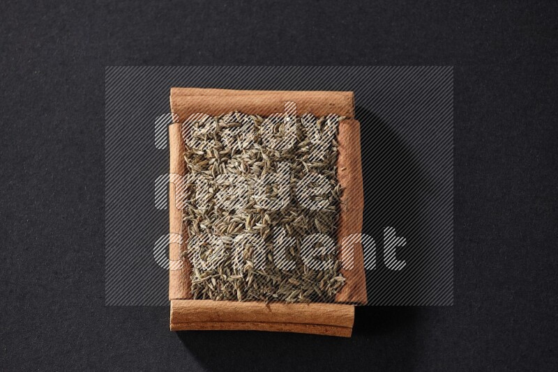 A single square of cinnamon sticks full of cumin on black flooring