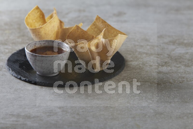 wonton cups with soy sauce ramkin on circle slate on grey textured counter top
