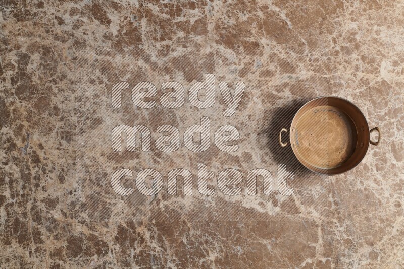 A small copper pan on beige marble background