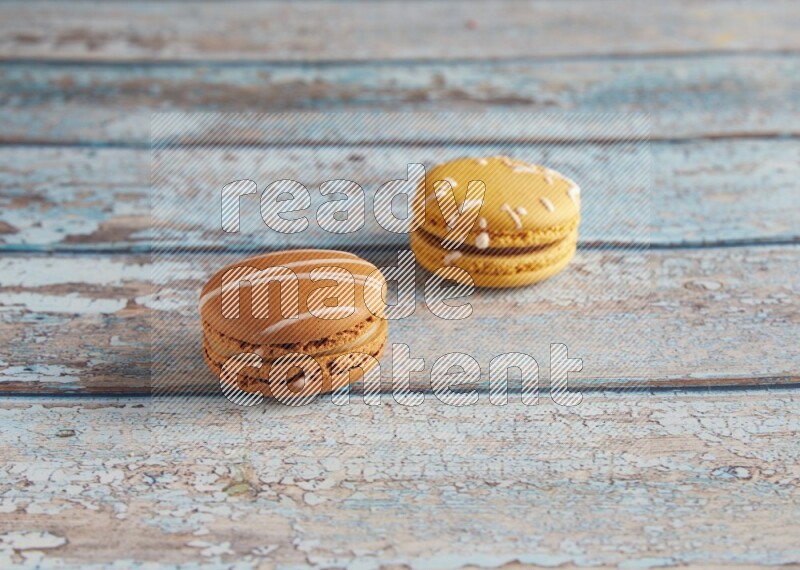 45º Shot of of two assorted Brown Irish Cream, and Yellow Piña Colada macarons on light blue background