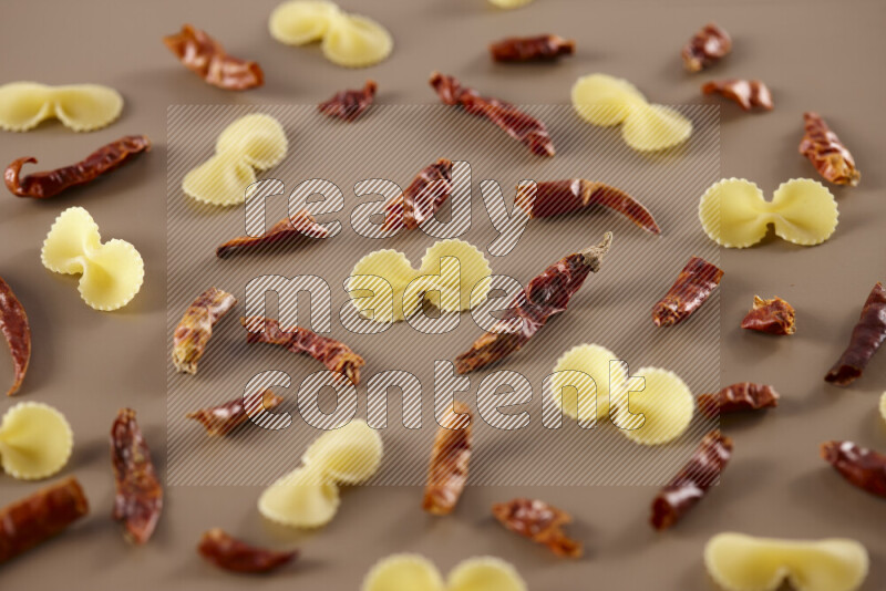 Raw pasta with different ingredients such as cherry tomatoes, garlic, onions, red chilis, black pepper, white pepper, bay laurel leaves, rosemary and cardamom on beige background