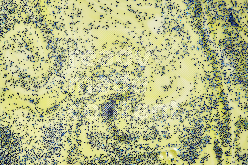 A close-up of sparkling blue glitter scattered on swirling yellow background