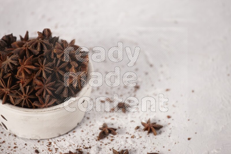 Star Anise in a white bowl and more of it sprinkled on white background