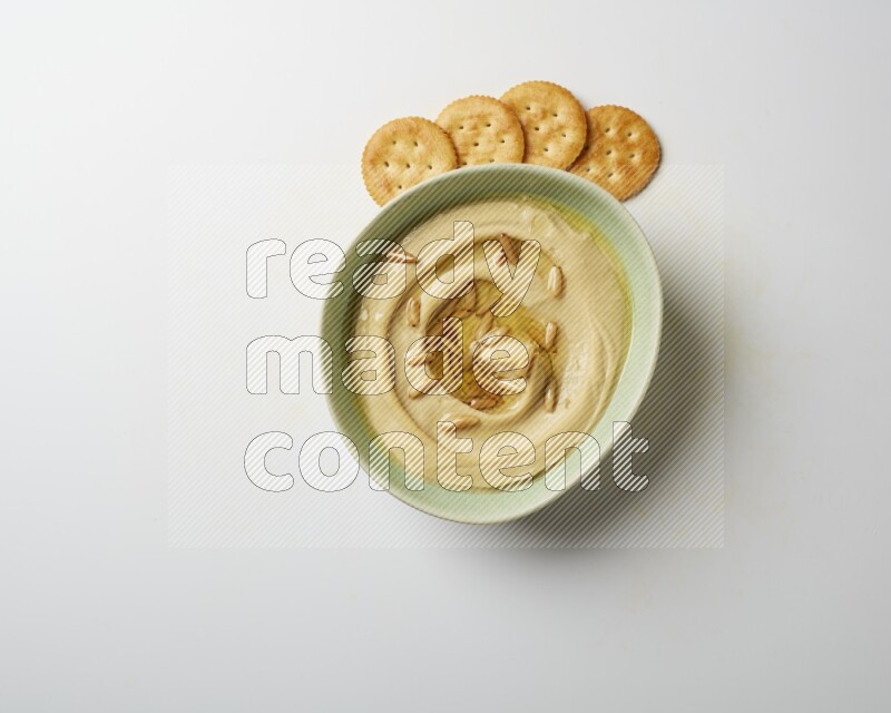 Hummus in a green plate garnished with pine nuts on a white background