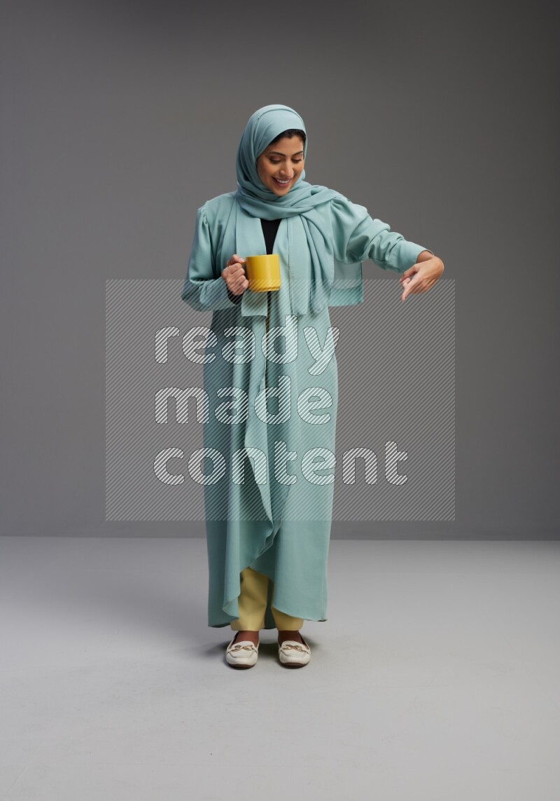 Saudi Woman wearing Abaya standing  holding a mug on Gray background
