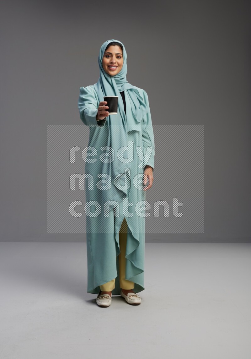 Saudi Woman wearing Abaya standing  holding paper cup on Gray background
