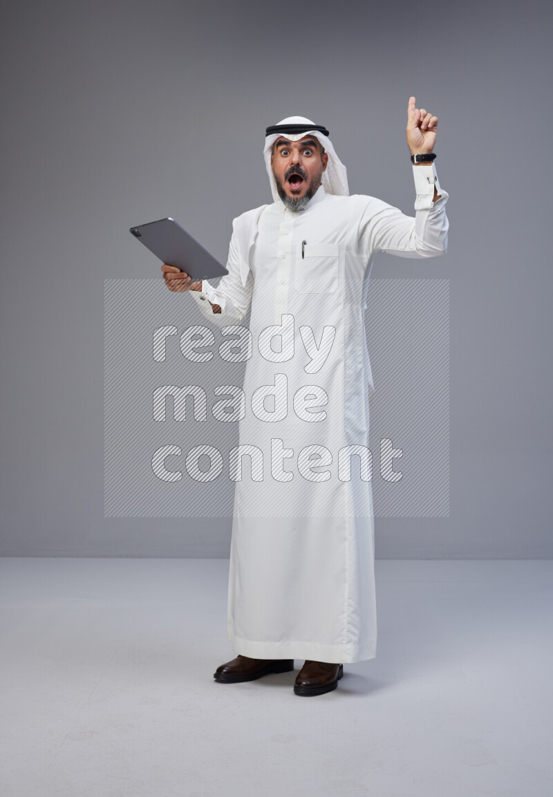 Saudi man Wearing Thob and white Shomag standing working on tablet on Gray background