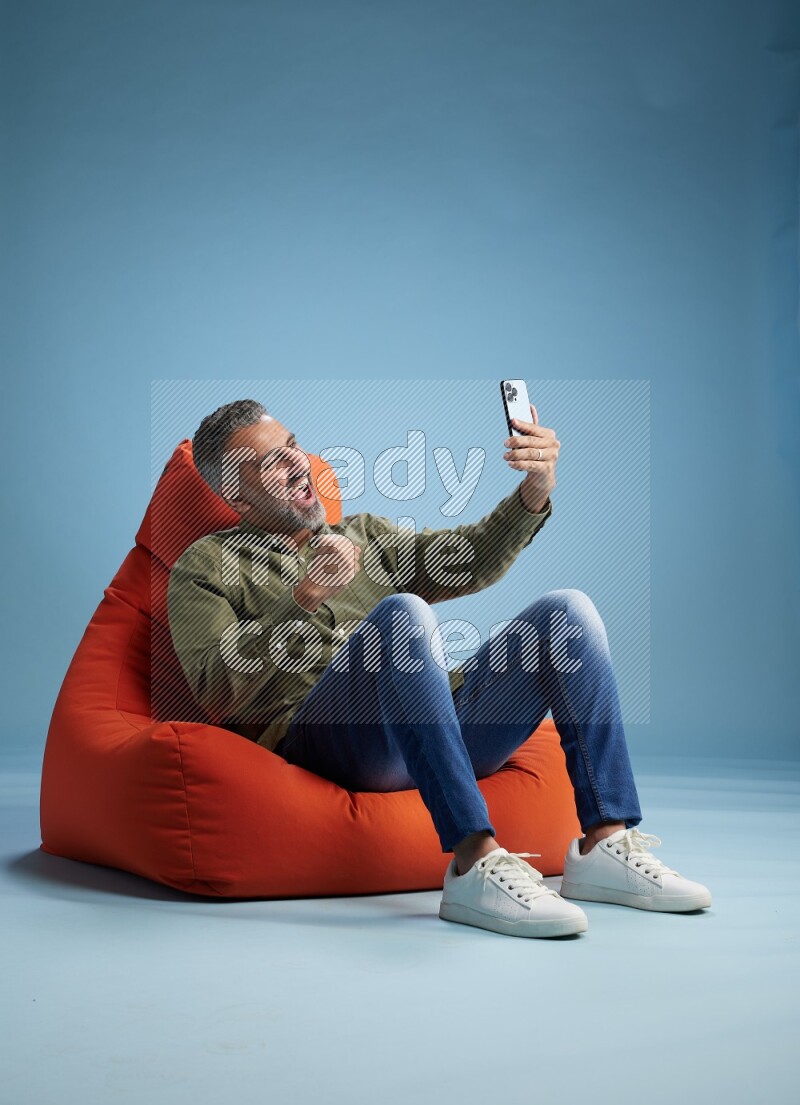 A man sitting on an orange beanbag and taking selfie