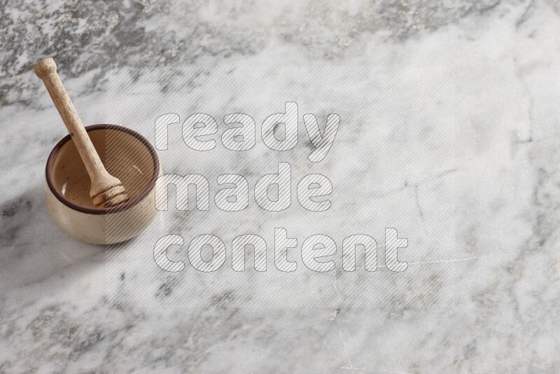 Beige Pottery oven bowl with wooden honey handle on the side with grey marble flooring, 65 degree angle