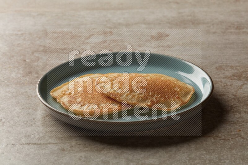 Two stacked plain pancakes in a blue plate on beige background