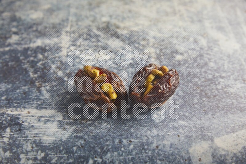 two pistachios stuffed madjoul dates on a rustic blue background