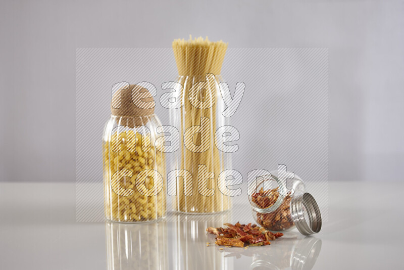 Raw pasta in glass jars with chilis on light grey background