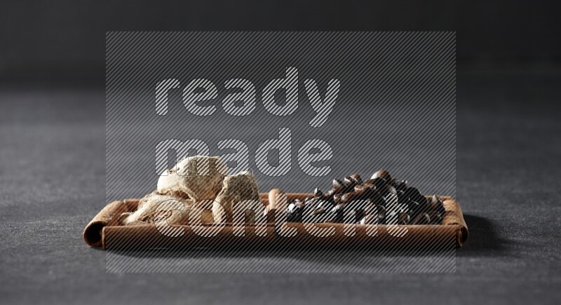 مربعان من أعواد القرفة ممتلئان بحبوب القهوة والزنجبيل المجفف علي خلفية سوداء