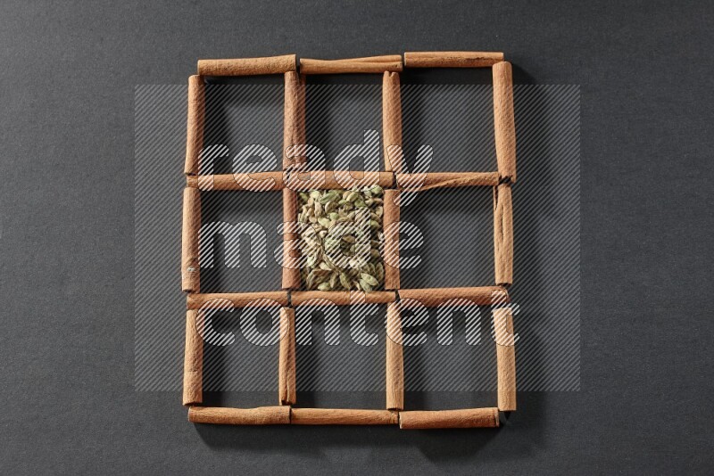 9 squares of cinnamon sticks full of cardamom in the middle surrounded by nutmeg, cinnamon, bay laurel leaves, cloves, cumin, dried ginger, dried basil and star anise on black flooring