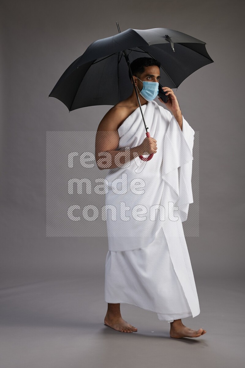 A man wearing Ehram and mask Standing holding umbrella on gray background on gray background